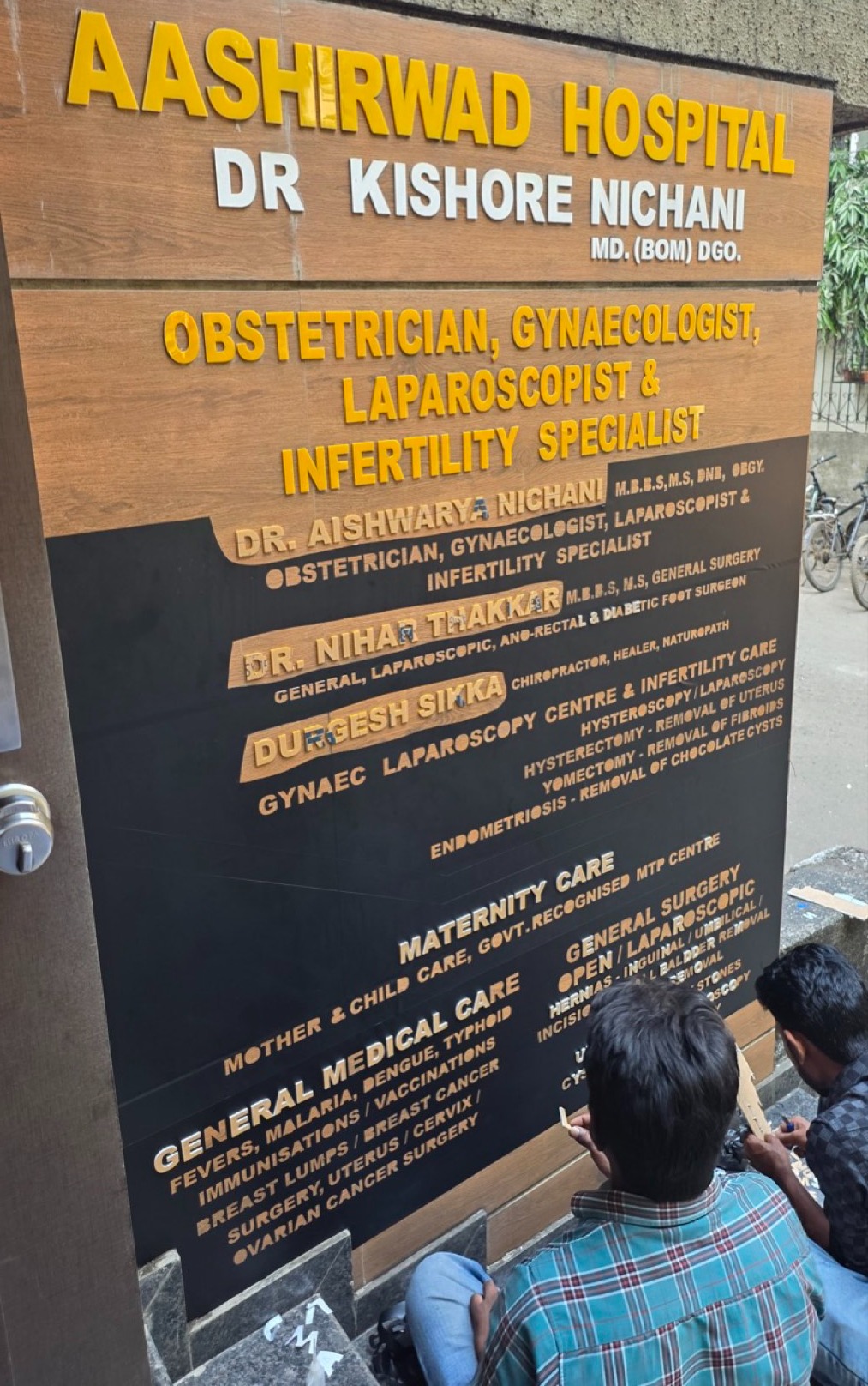 Sign painters adding Dr. Aishwarya Nichani's name to the Aashirwad Hospital board in 2025